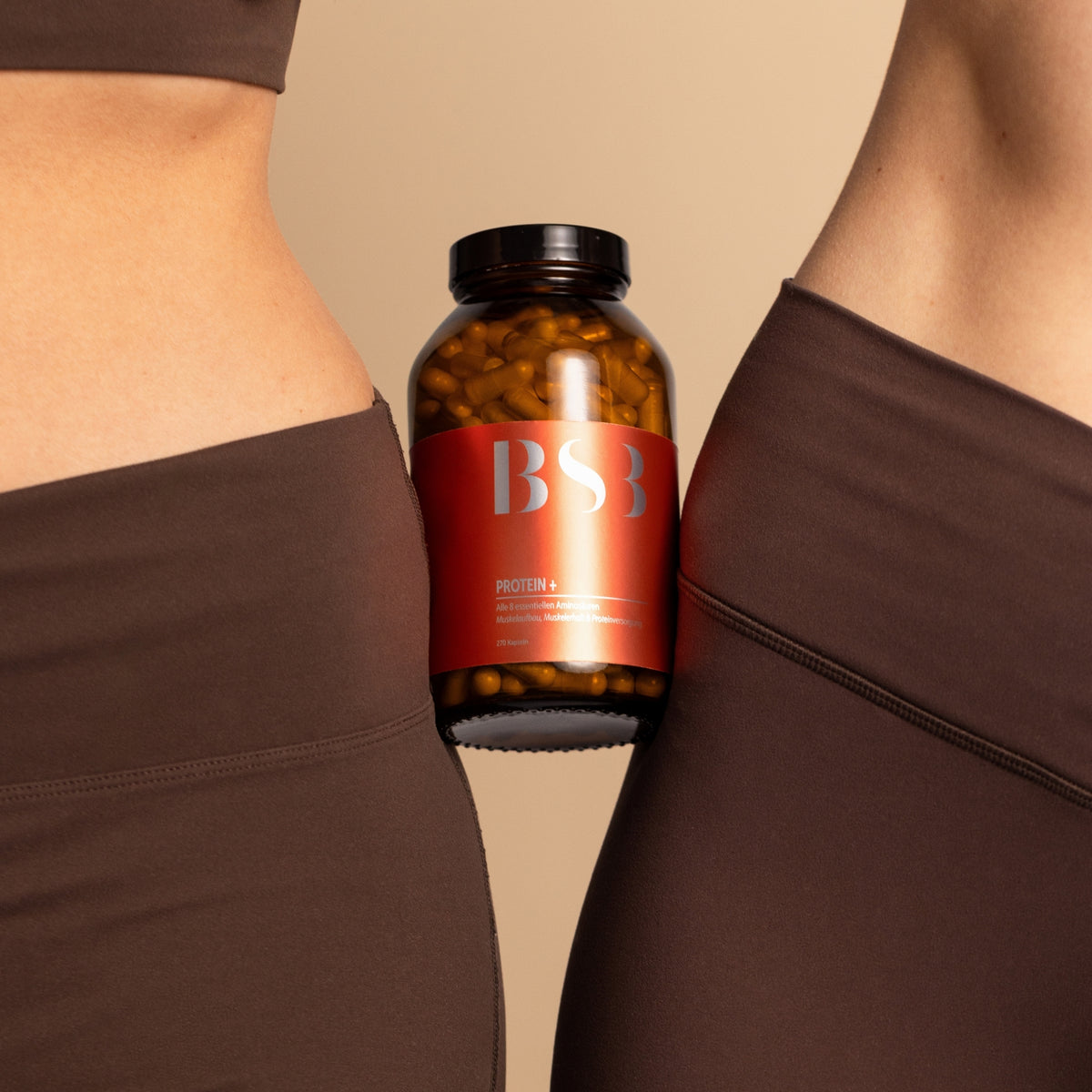 Zwei Frauen in Sportkleidung mit einem Glas Protein+ zwischen sich